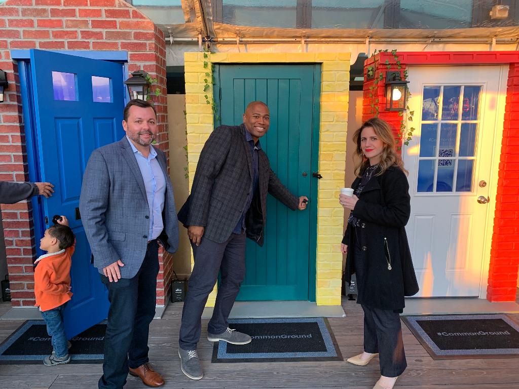 NFL Legend Shaun Alexander poses with two people as they open a door at a pop-up event
