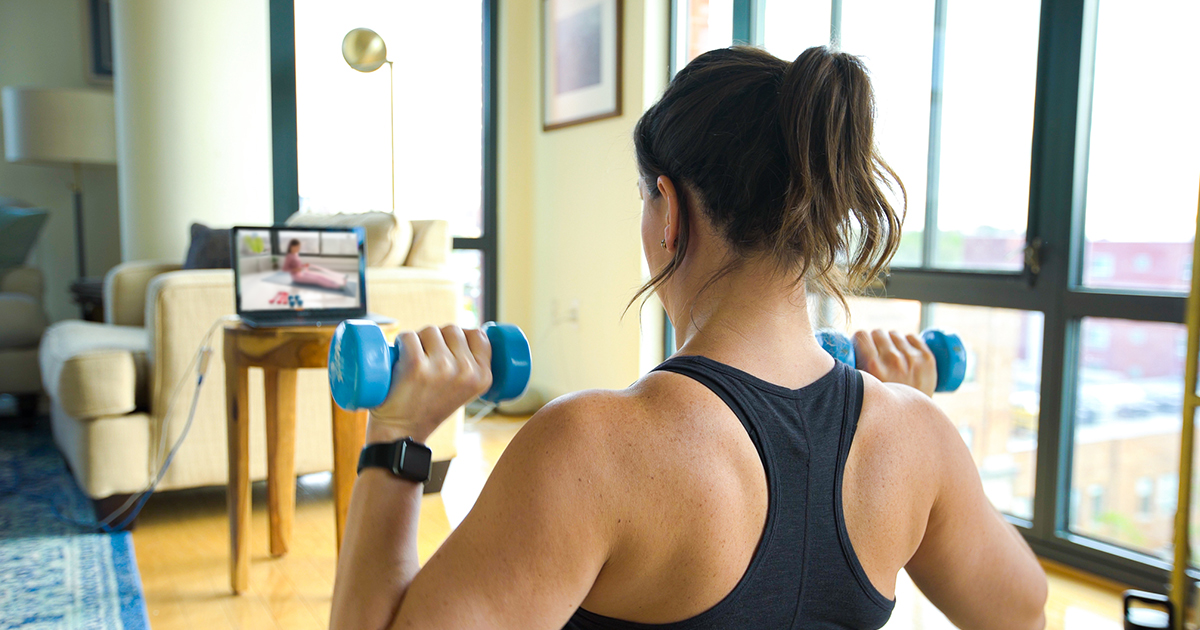 A woman following a home workout video with dumbbells in her hand