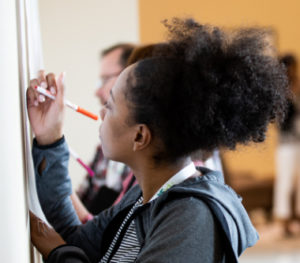 Young girl with afro hair writing on a whiteboard.