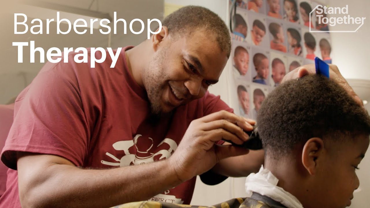 A man in a maroon shirt with a joyful expression is cutting the hair of a young boy in a barbershop.