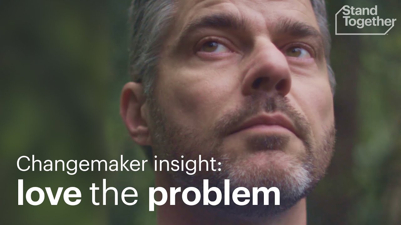 Close-up of a man's face looking contemplative against a blurred green background, with the text "Changemaker insight: love the problem" overlaying the image.