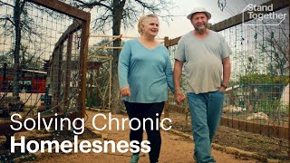 A man and woman walking hand in hand outdoors with a fence in the background, text "Solving Chronic Homelessness."