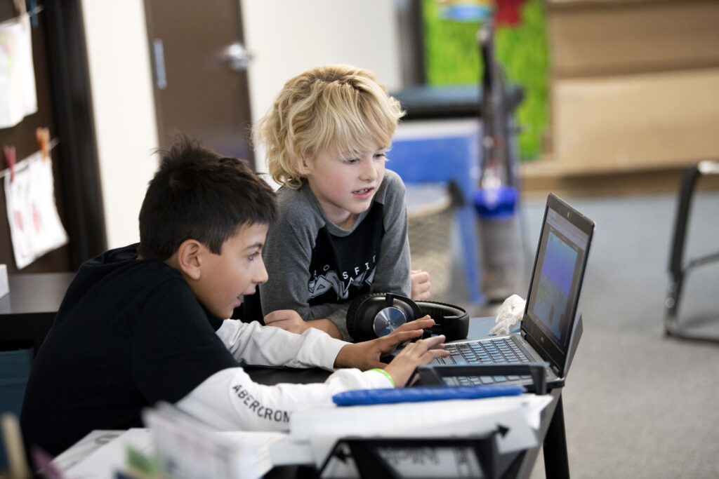 Two kids looking intently at a computer at school