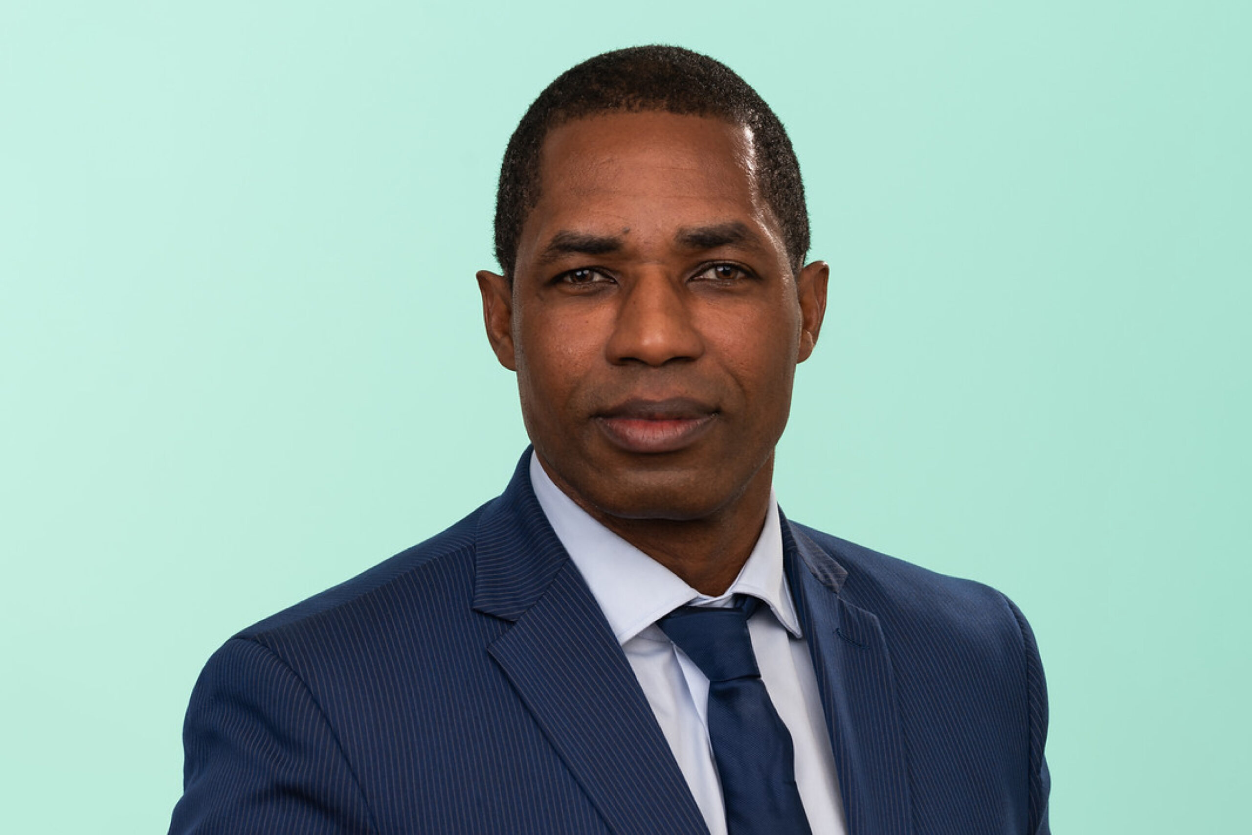 Man in blue suit and tie against a mint green background.